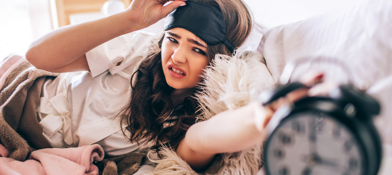 Frau mit Schlafmaske im Bett greift zum Wecker. Frau mit Schlafmaske im Bett greift zum Wecker.
